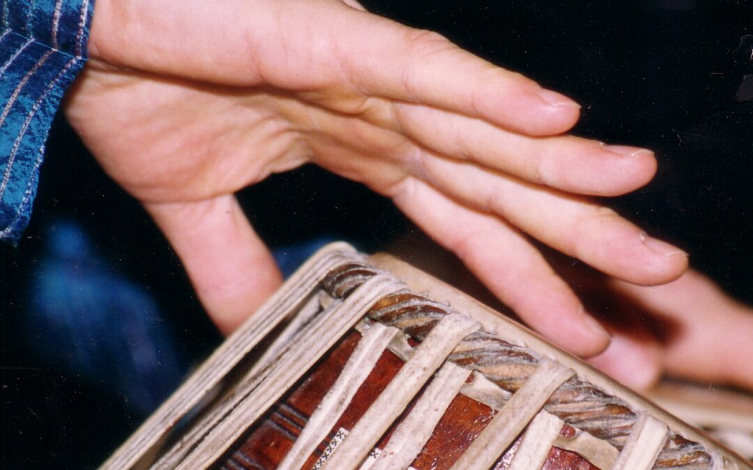 Hands on tabla, mid-stroke — the moment of contact between drummer and instrument
