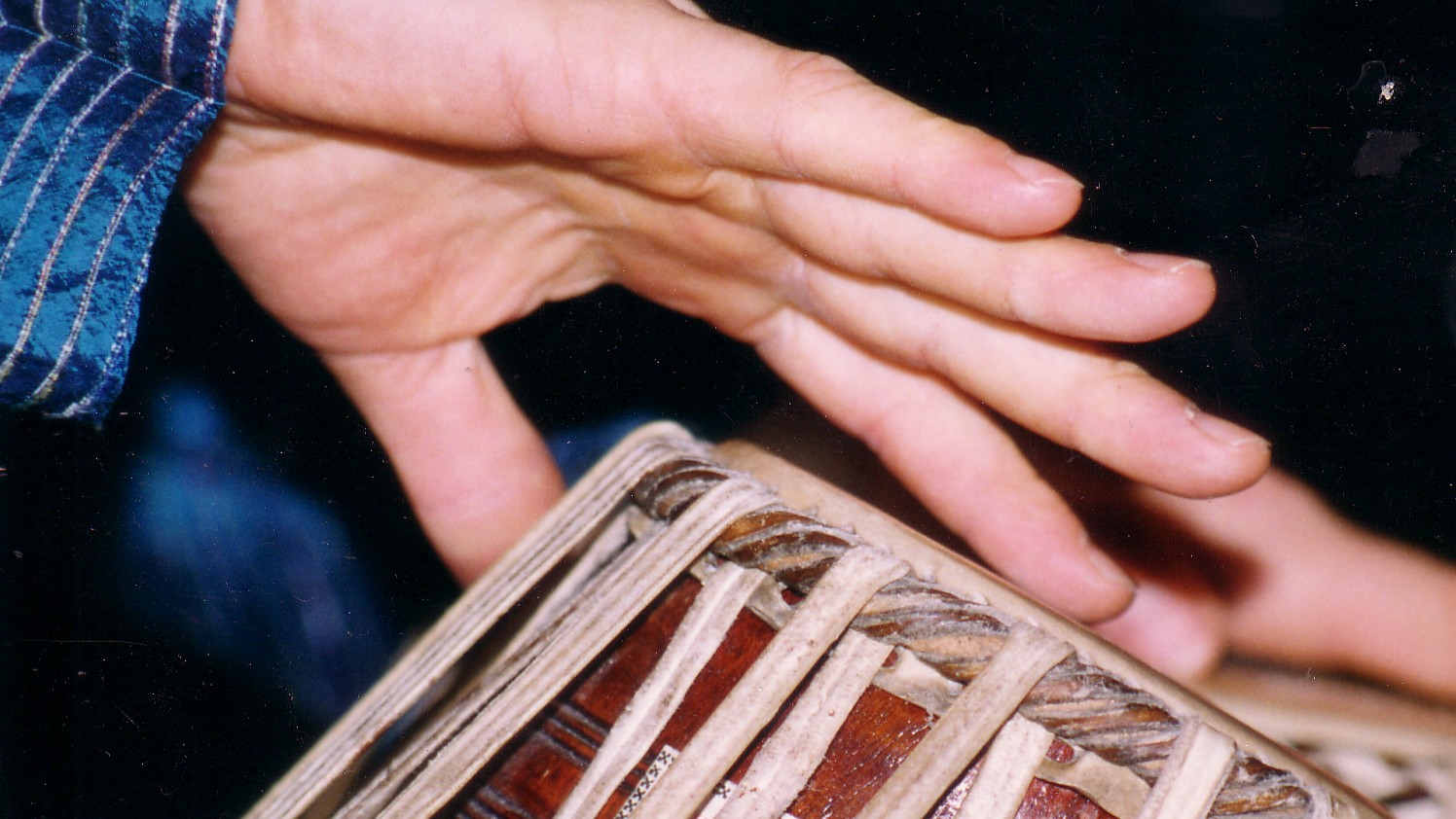 Hands on tabla, mid-stroke — the moment of contact between drummer and instrument